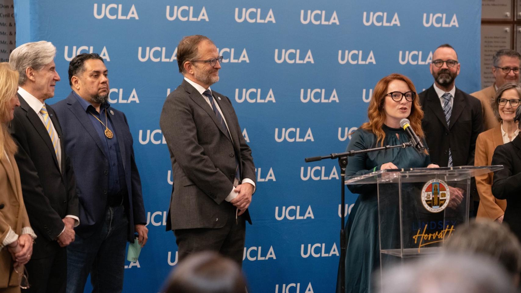 UCLA Chancellor Julio Frenk watches as County Supervisor Lindsey Horvath speaks at the podium